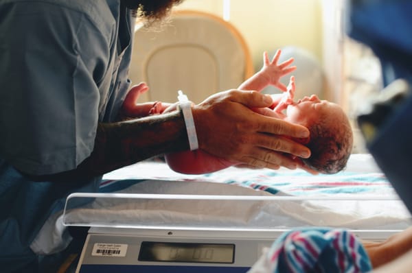 man putting baby on scale at a hospital