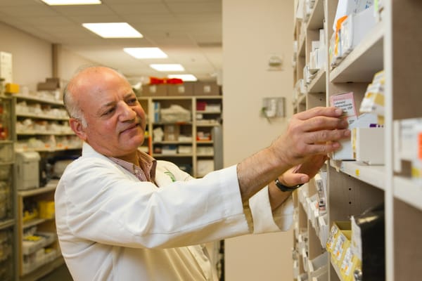 A pharmacist is selecting a drug from a pharmacy display case.