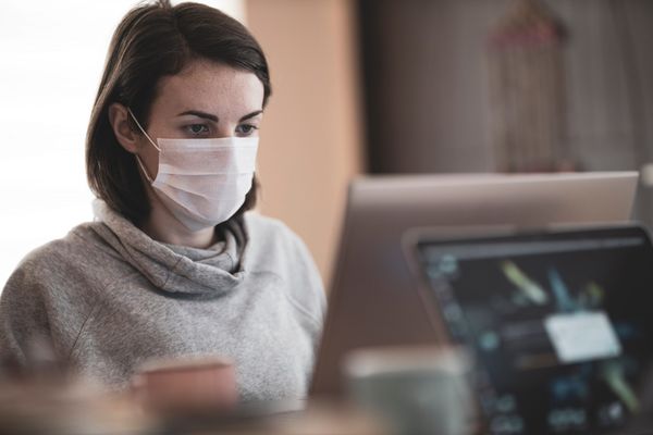 a woman working on a computer and wearing a mask